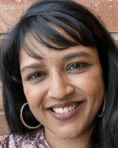 A close-up photo of Seema N. Patel smiling with dark hair and hoop earings